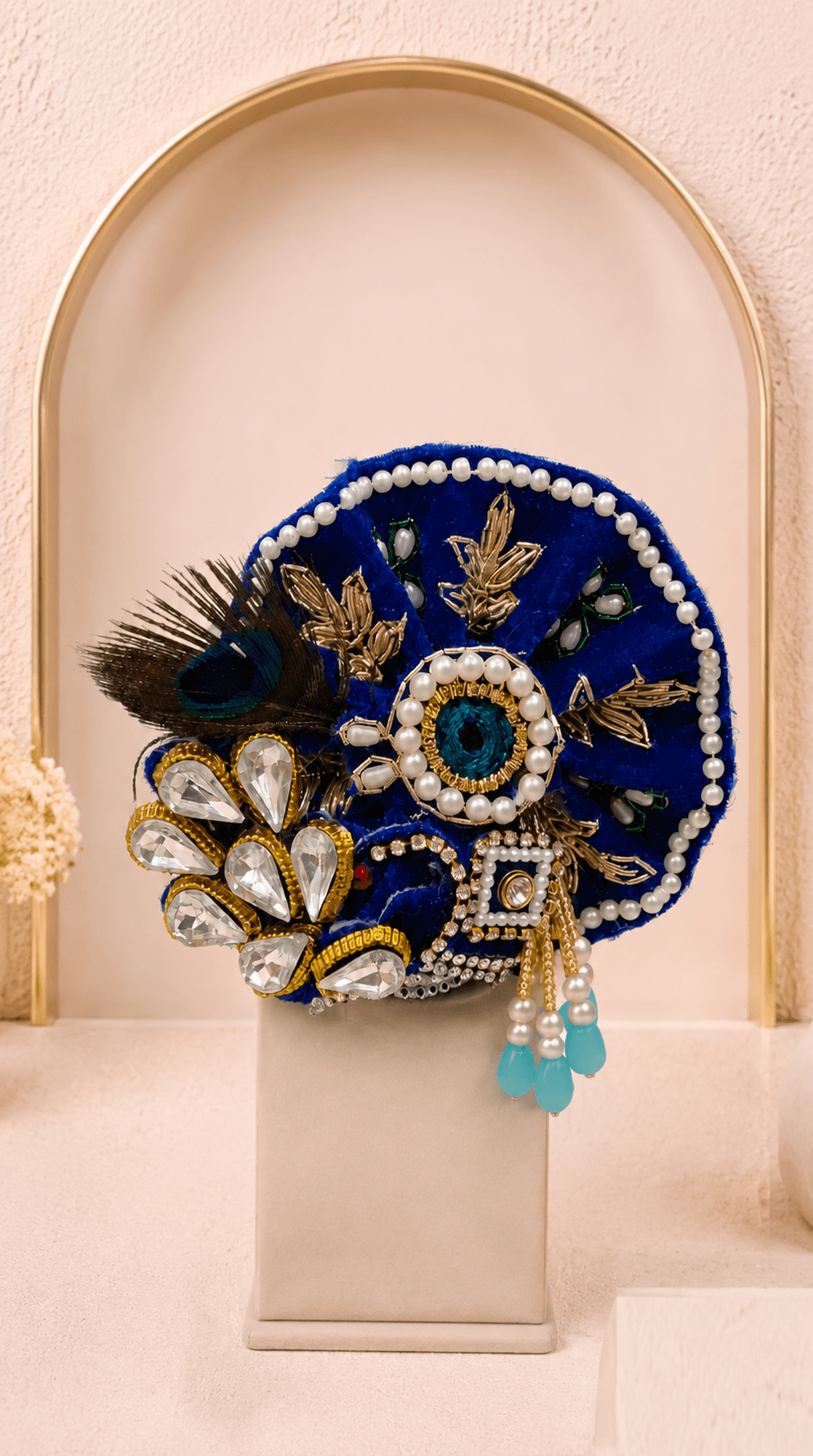Designer mukut from the Neelambar Set featuring royal blue fabric, golden embroidery, pearl detailing, peacock feather and handcrafted embellishments for Laddu Gopal Ji